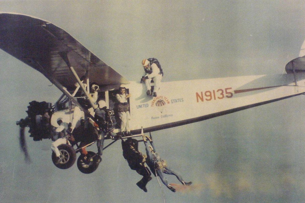 United States parachute plane with seven skydivers hanging on the the outside during flight.