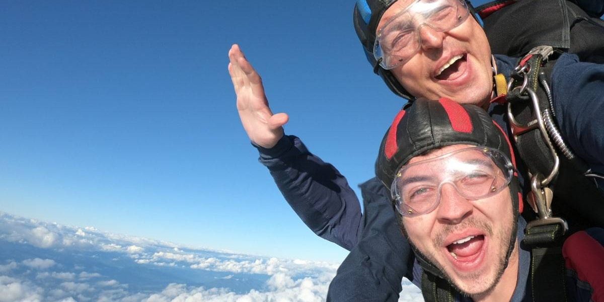 Young, male, tandem student making a "woohoo" face with while clouds below him.