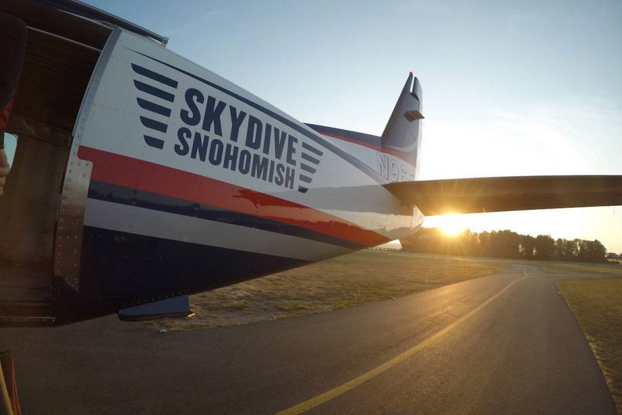 Blue, White, and Red Skydive Snohomish plane on the runway with sun in the background.