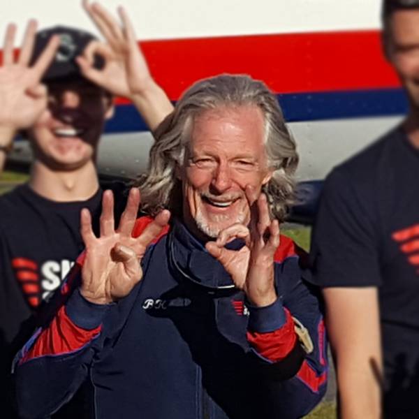 Bill Kelly smiling next to air plane and the rest of the Skydive Snohomish crew.