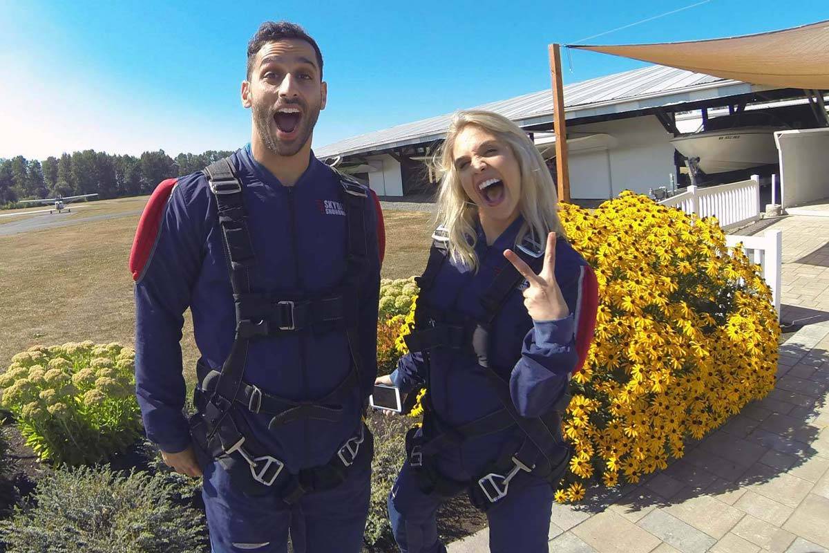 Female with blond hair and gentle men with beard excited to go skydiving with yellow flowers in the background.