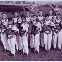 Ten skydivers holding helmets behind older Skydive Snohomish plane.