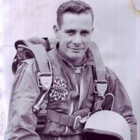 Headshot of gentlemen sitting while wearing skydiving gear and holding a helmet.