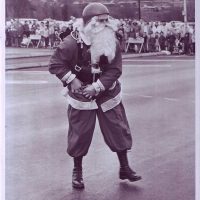 Gentlemen smiling while wearing santa outfit and beard with helmet on.