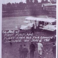 Spectators standing around and watching people get on airplane.