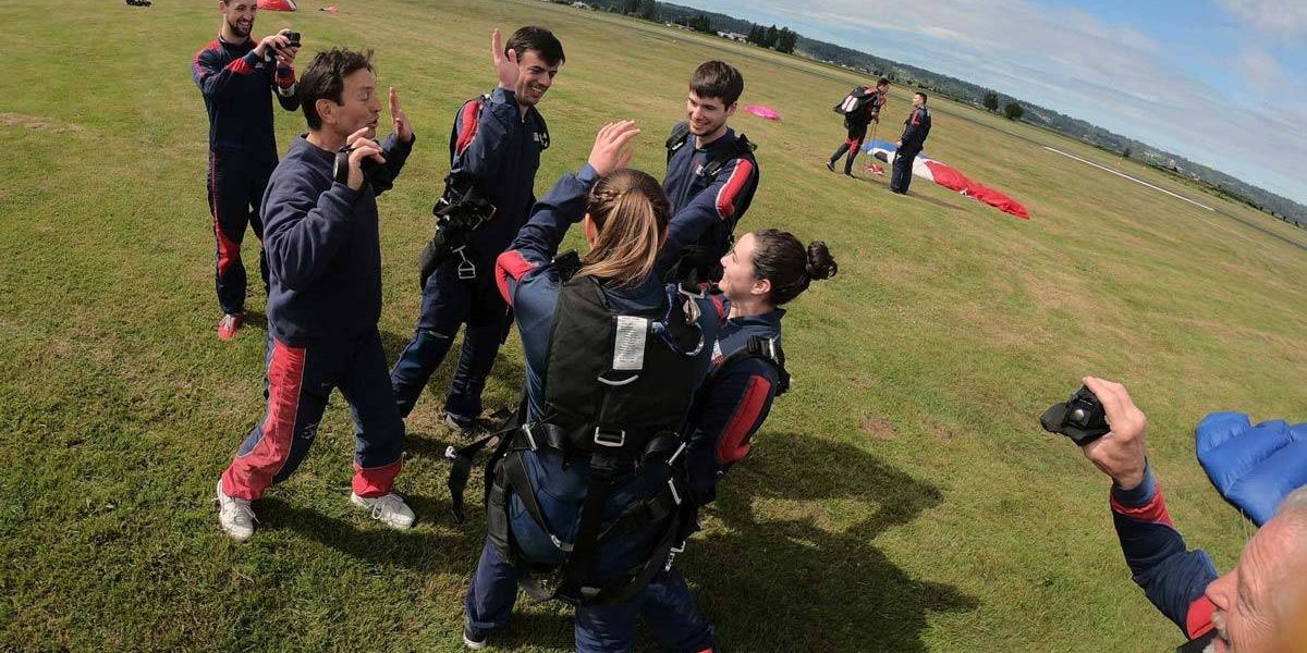 Group of people celebrating post skydive on the green grass landing area.