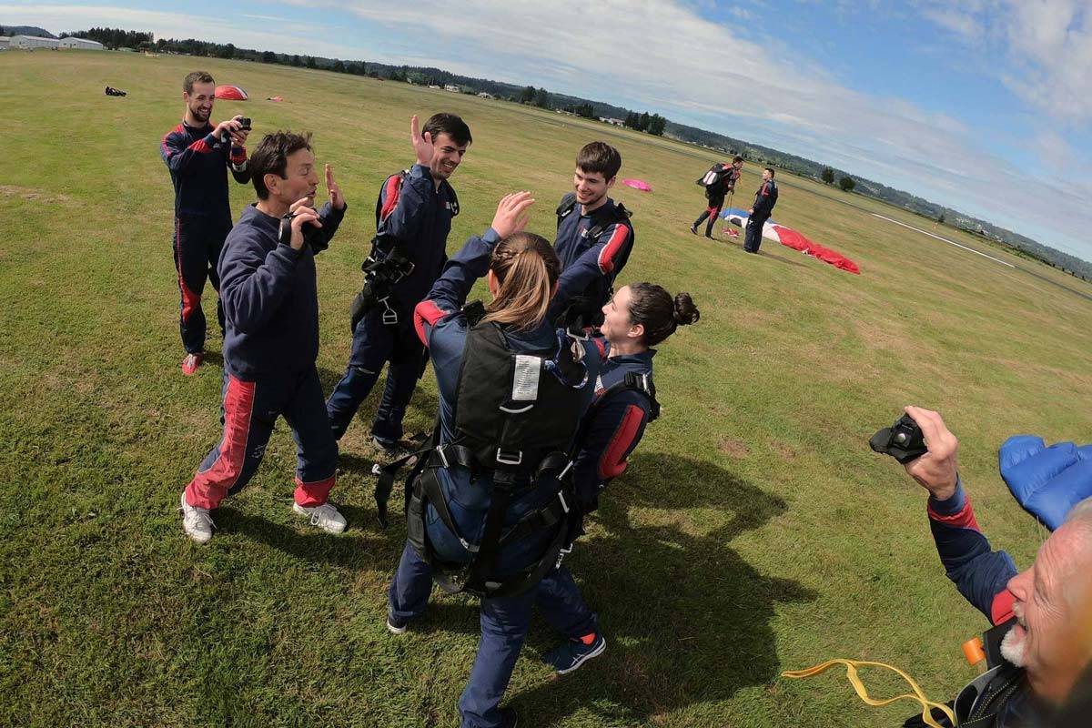 Group of people celebrating post skydive on the green grass landing area.