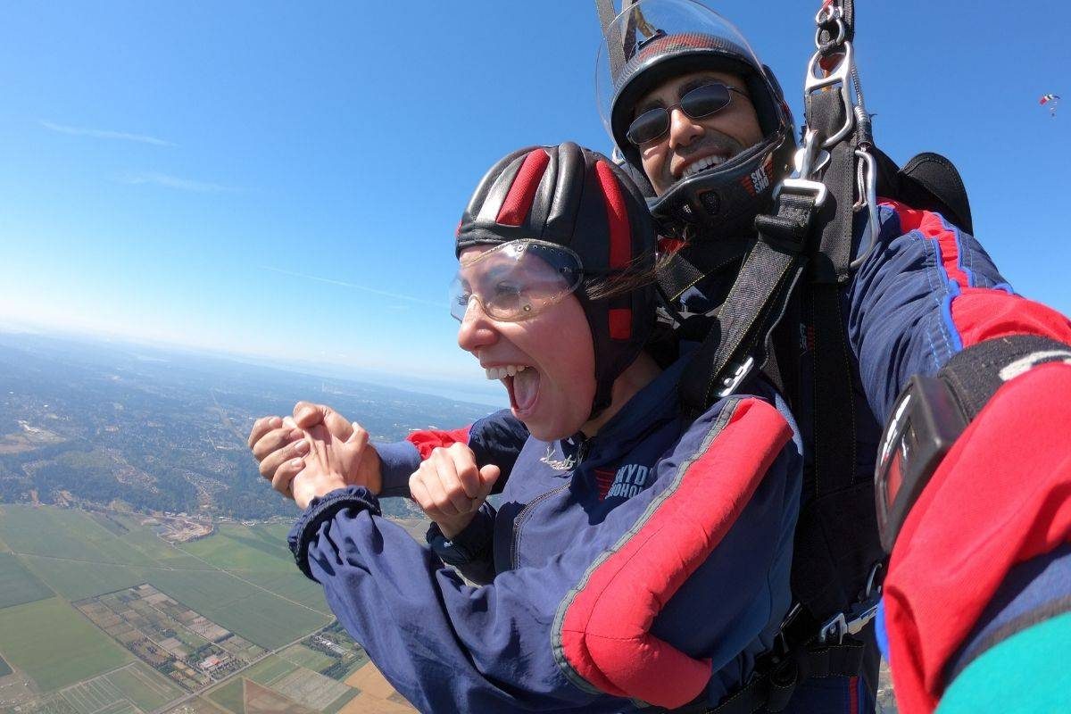 Young women wearing Red and Blue skydiving gear is excited to be in free fall with tandem instructor