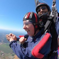 Young women wearing Red and Blue skydiving gear is excited to be in free fall with tandem instructor