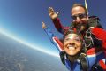 Young female skydiver smiles while in free fall with tandem instructor