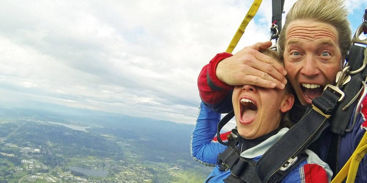 Tandem instructor playfully covering students eyes while skydiving.