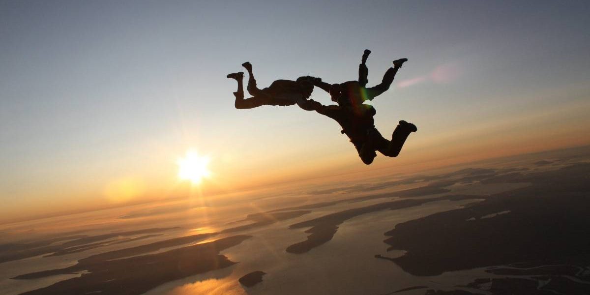 Three experienced skydivers in formation during free fall with the sun shining in the background.