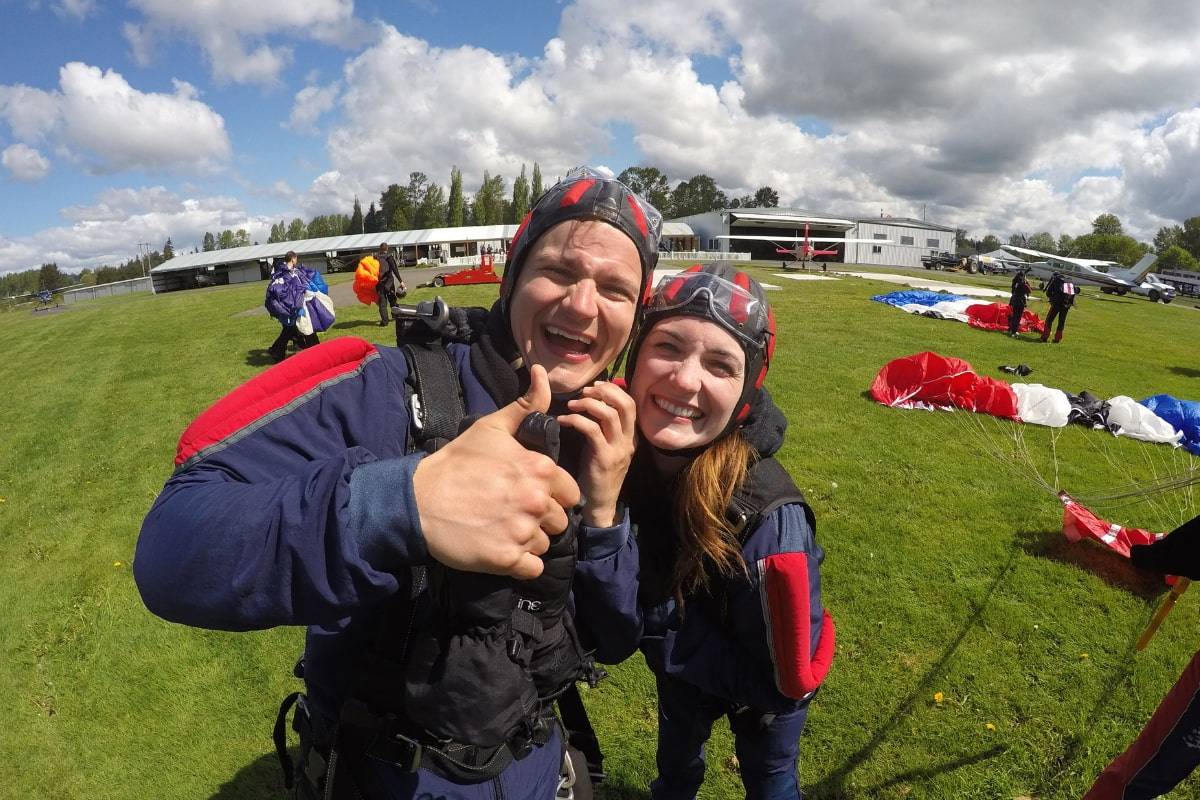 Girl and guy smiling post skydive with Blue, White, Red, and Black canopy in the background.