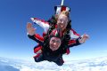 Female tandem student smiling during free fall above white clouds.