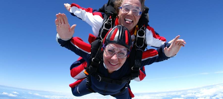 Female tandem student smiling while skydiving about the clouds.