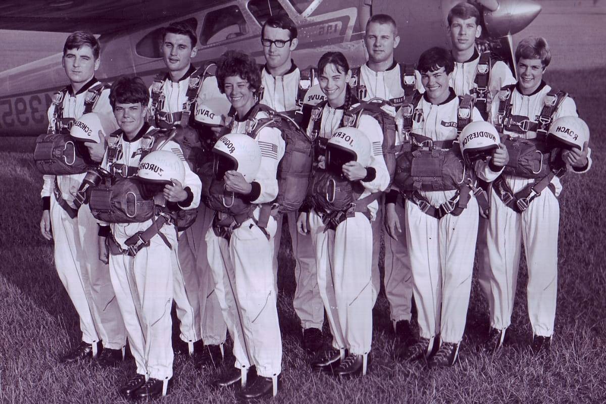Ten skydivers holding helmets behind older Skydive Snohomish plane.