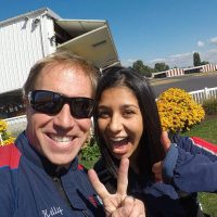 Female tandem skydiver with black hair smiling and giving thumbs up with tandem instructor.