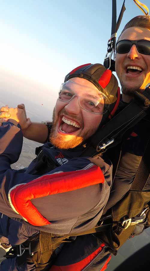 Student and tandem instructor with black sunglasses on in the air smiling.