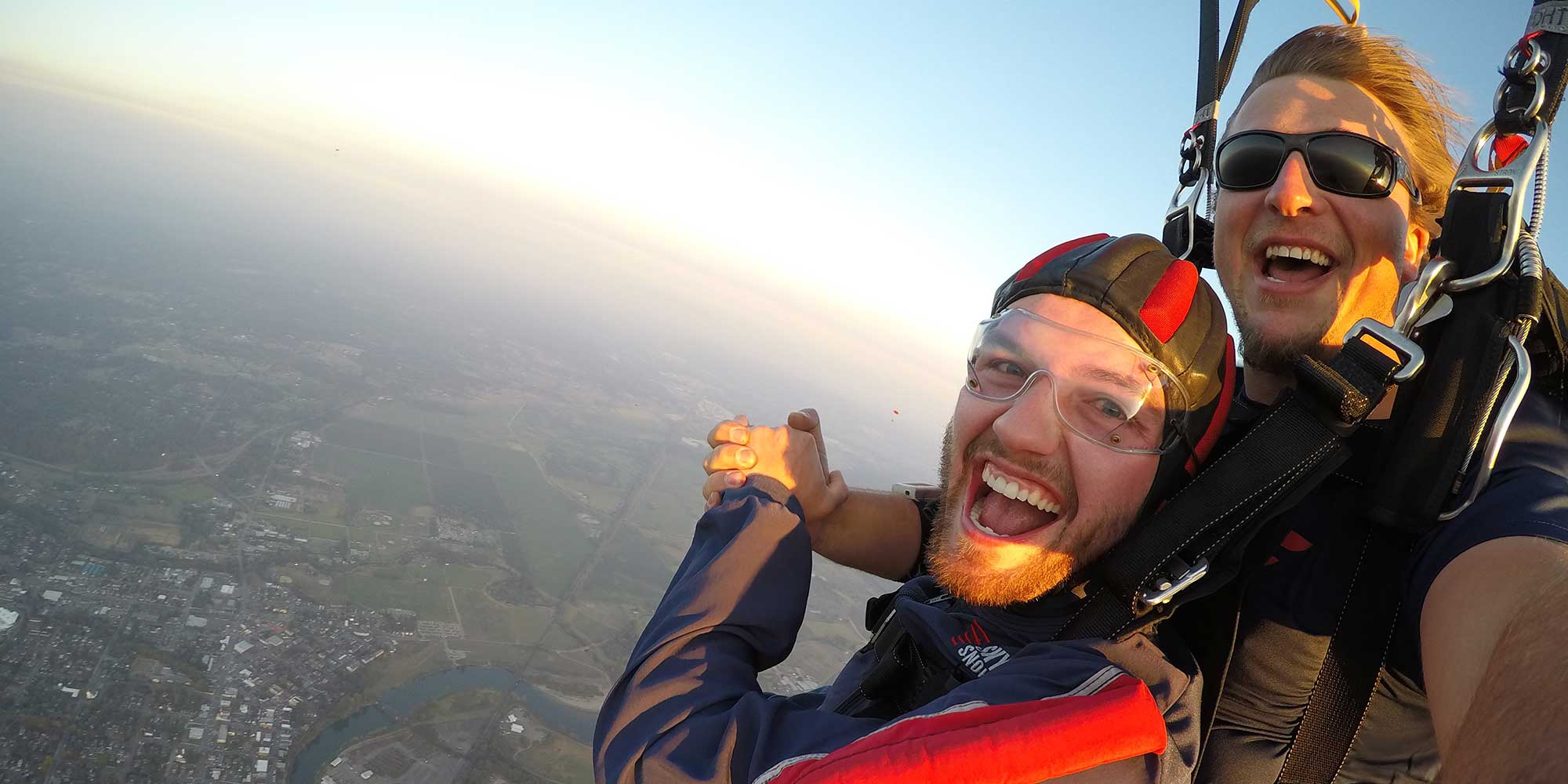 Student and tandem instructor with black sunglasses on in the air smiling.