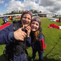 Young male and female smiling while male gives thumbs up post skydive
