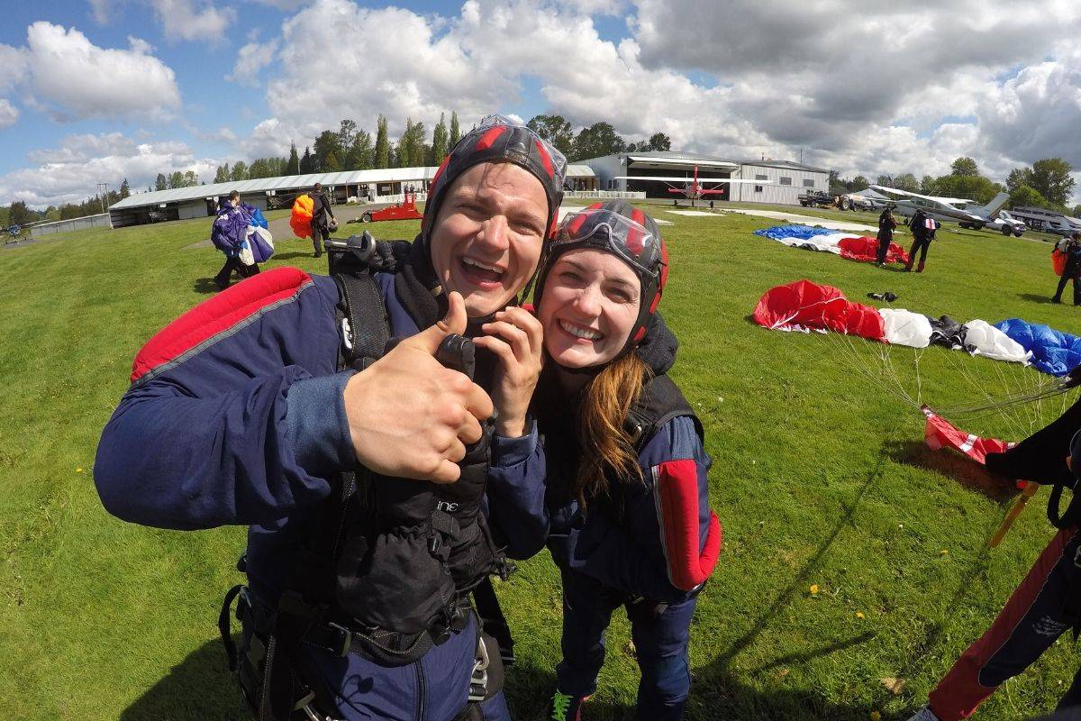 Young male and female smiling while male gives thumbs up post skydive