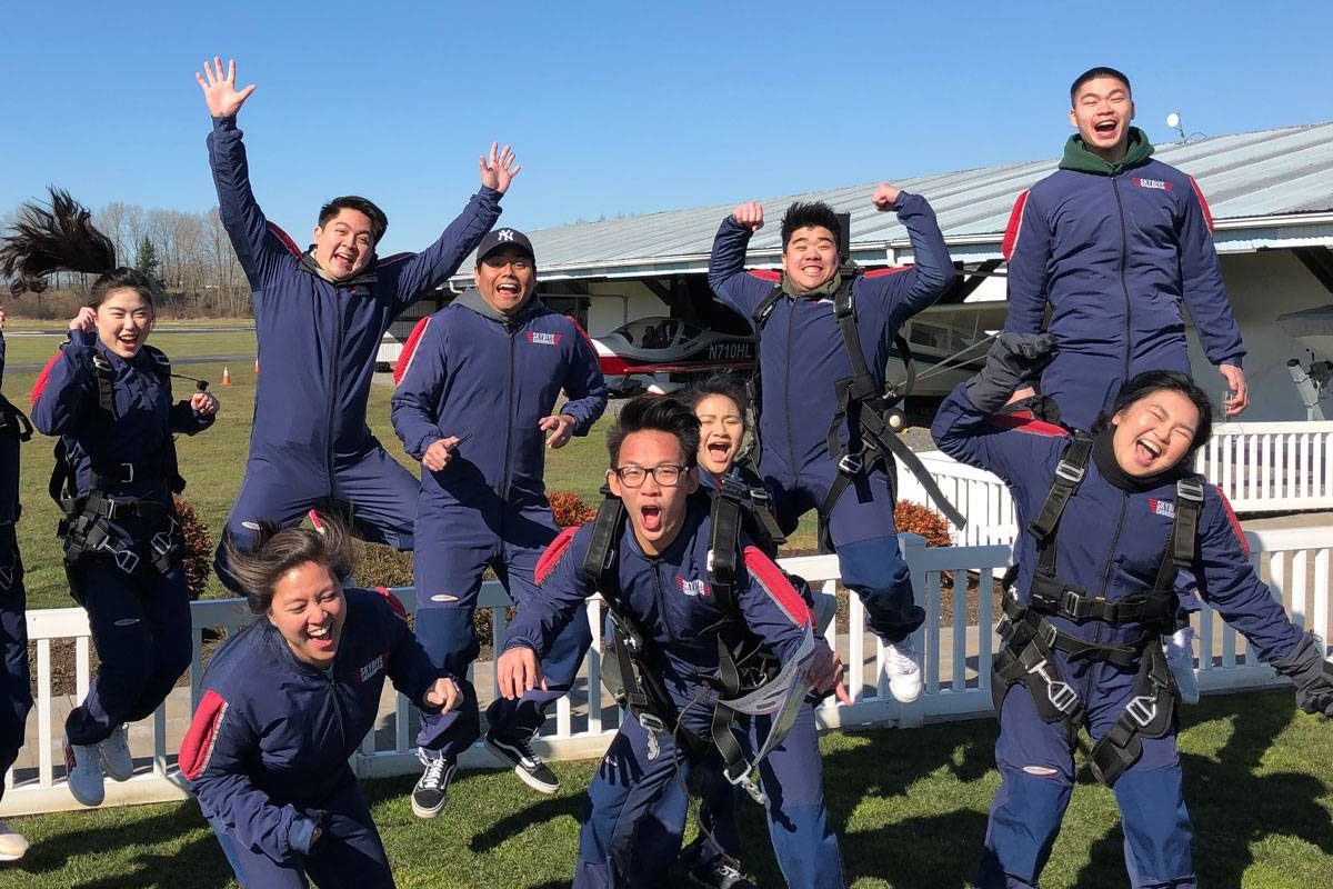 Eleven tandem skydivers jumping in the air excited to go skydiving.