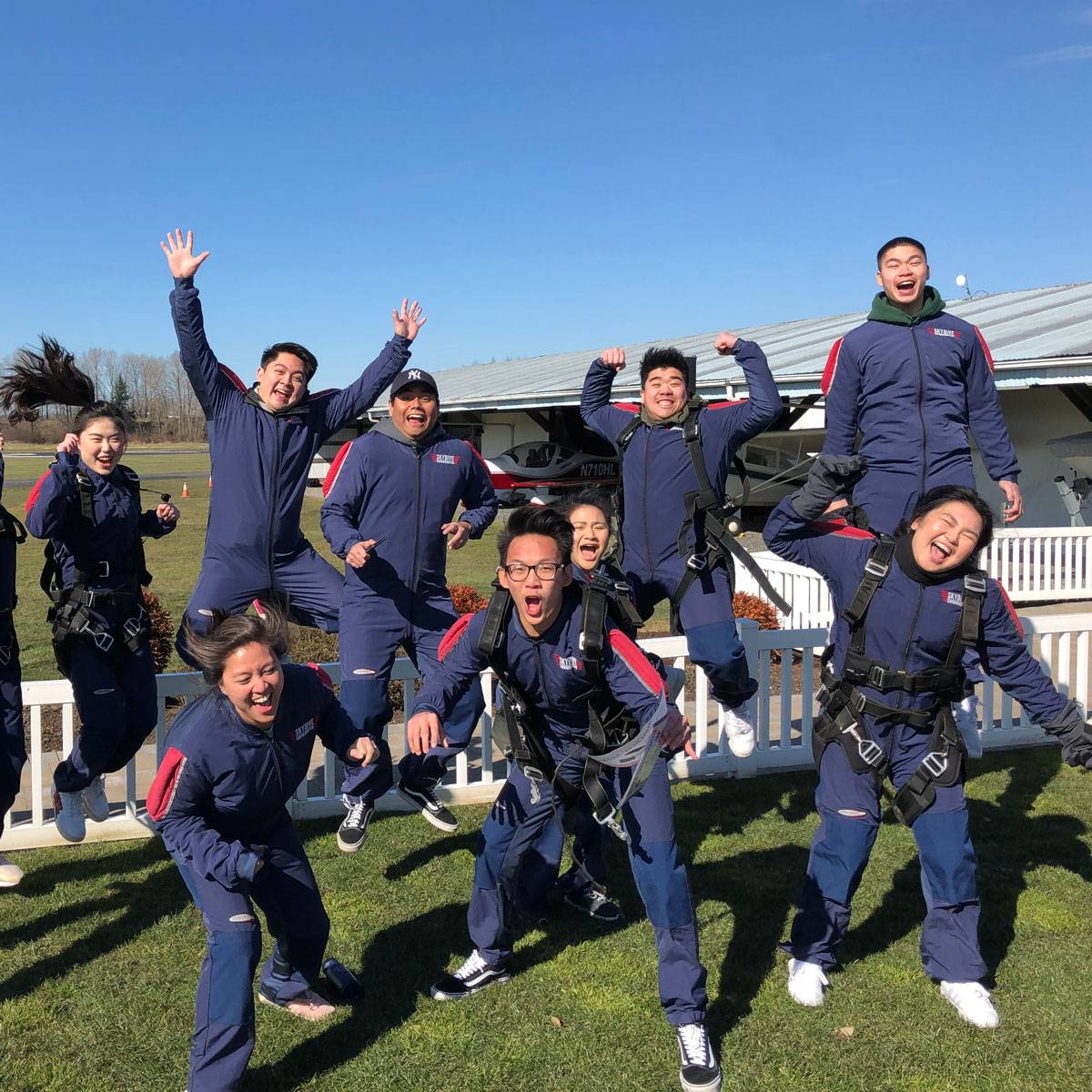 Eleven tandem skydivers jumping in the air excited to go skydiving.