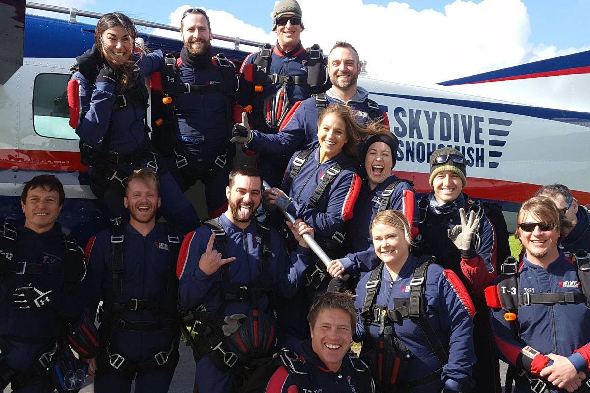 Skydive Snohomish staff smiling in front of Red, White, Blue and Black airplane.