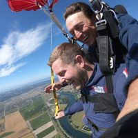 Young male tandem student smiling while skydiving.
