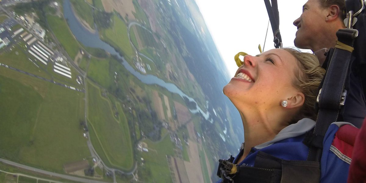 Female tandem skydiver excited floating down towards green land below.