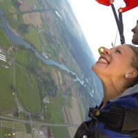 Female tandem skydiver excited floating down towards green land below.