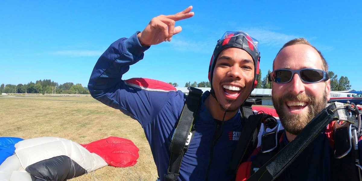 Tandem instructor and student excited post skydive with black, white, red, and white canopy in the background.