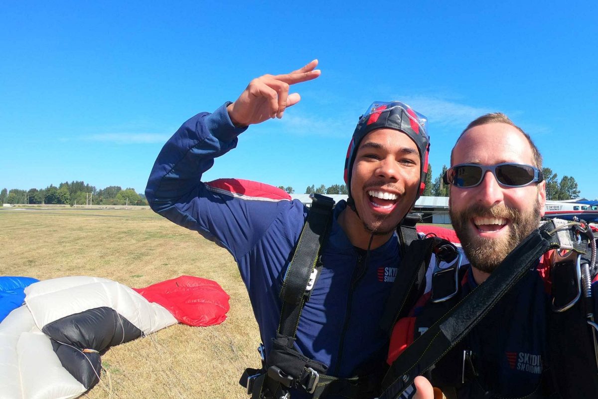 Tandem instructor and student excited post skydive with black, white, red, and white canopy in the background.