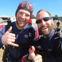 Young male tandem student and instructor giving thumbs up post landing.