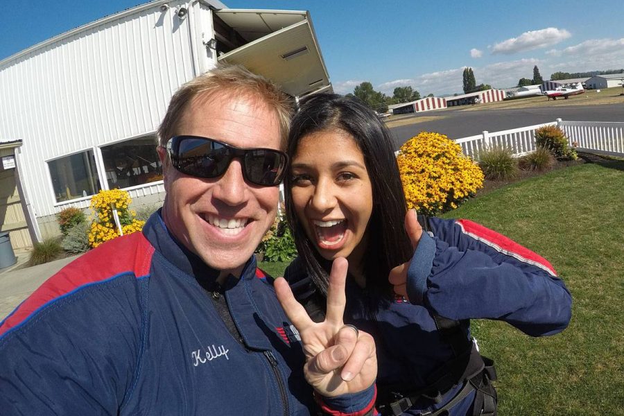 Female tandem skydiver with black hair smiling and giving thumbs up with tandem instructor.