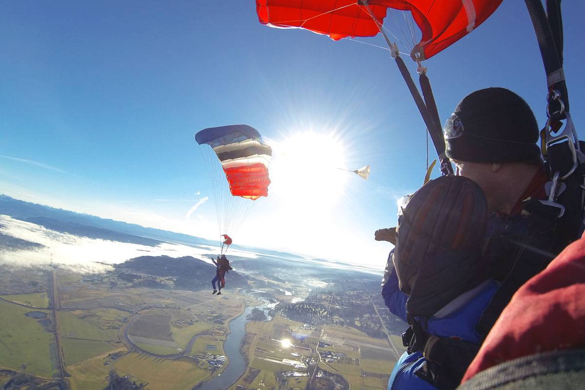 Two sets of tandem skydivers enjoying the view with Red, White, Blue and Black canopies above them.