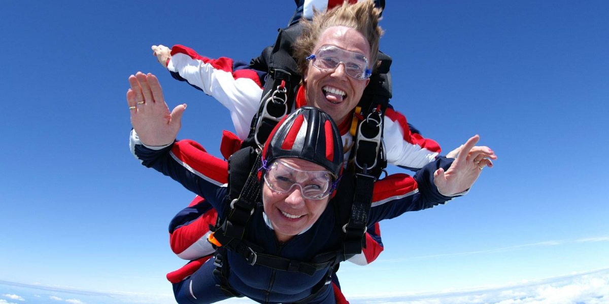 Women and tandem instructor in smiling in free fall surrounded by clouds.